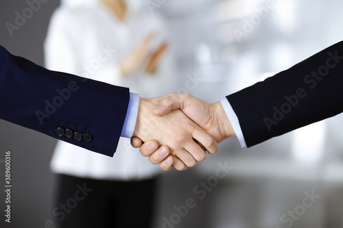 Business people shaking hands at meeting or negotiation, close-up. Group of unknown businessmen and a woman standing in a modern office. Teamwork, partnership and handshake concept