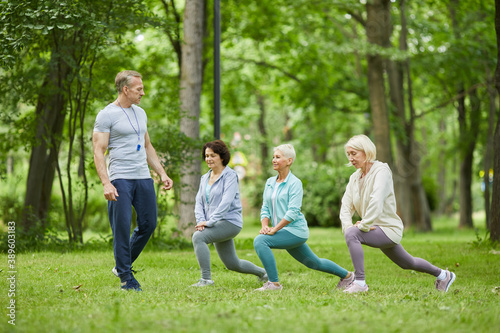 Wide shot of three good-looking senior women having workout in city park with trainer looking at them