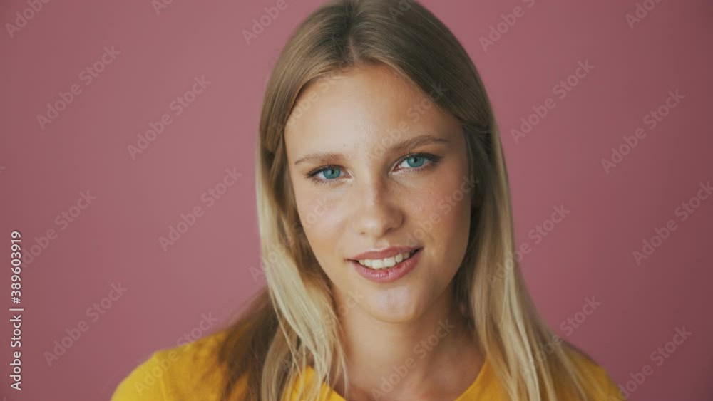 A beautiful blonde woman is sending an air kiss to the camera standing isolated over a pink background in the studio A beautiful blonde woman is sending an air kiss to the camera standing isolated over a pink background in the studio