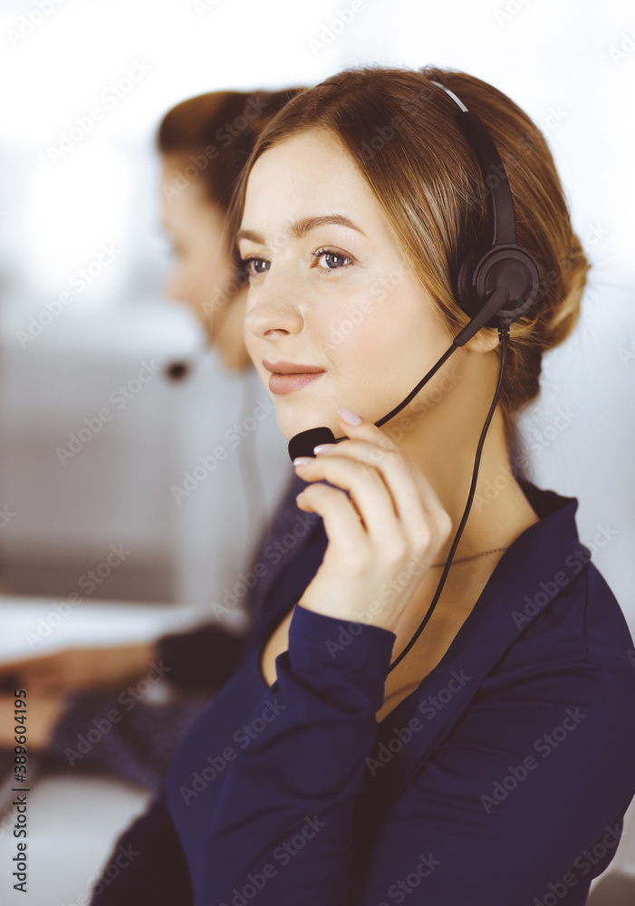 Two busineswomen have conversations with the clients by headsets, while sitting at the desk in a modern office. Diverse people group in a call center. Telemarketing and customer service Two busineswomen have conversations with the clients by headsets, while sitting at the desk in a modern office. Diverse people group in a call center. Telemarketing and customer service