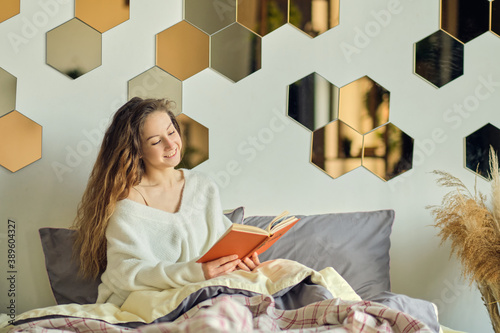 beautiful young woman in a warm knitted sweater reads a book. lazy weekend on a winter morning.