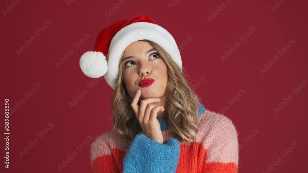 Young thinking positive cute woman in christmas santa hat isolated over red wall background Young thinking positive cute woman in christmas santa hat isolated over red wall background