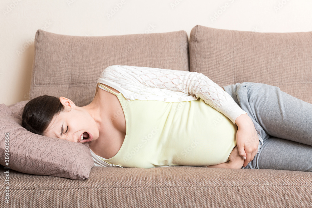 Beautiful pregnant woman suffering belly ache lying on a sofa at home Beautiful pregnant woman suffering belly ache lying on a sofa at home