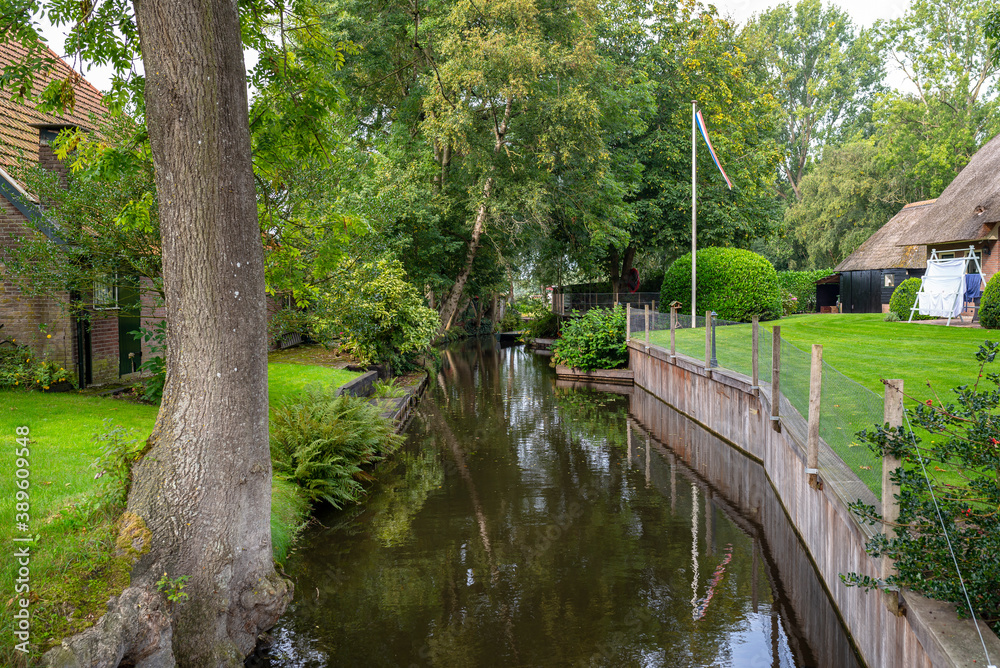 A canal flowing between buildings in a famous village in the Netherlands, visible trees and flowers in the gardens. A canal flowing between buildings in a famous village in the Netherlands, visible trees and flowers in the gardens.