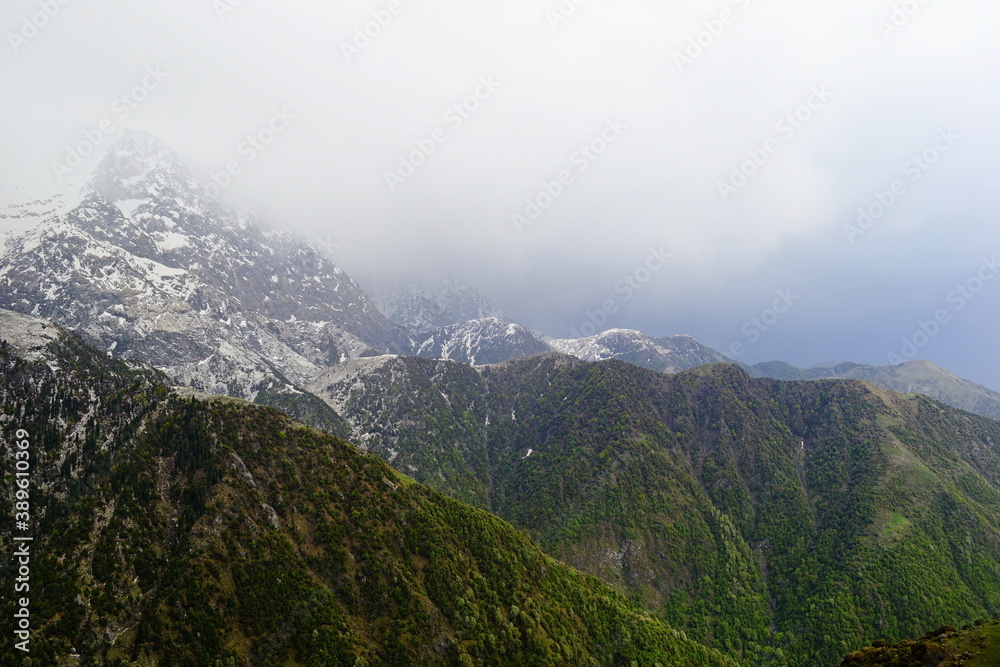Himalayan Mountains with snow on the top and ranges with green gras and trees. View from Triund Hill, Himachal Pradesh, India