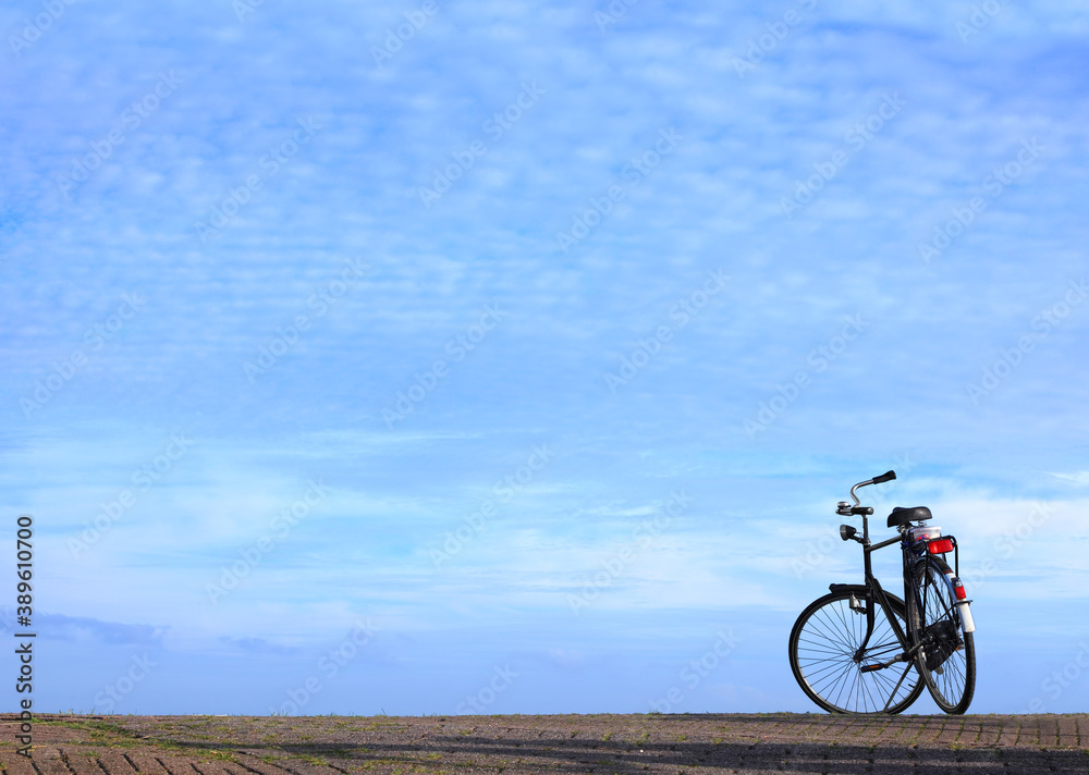 Bicycle parked on cobble stone road against magnificent blue sky over calm expanse on a sunny day. Netherlands. Minimalist image Bicycle parked on cobble stone road against magnificent blue sky over calm expanse on a sunny day. Netherlands. Minimalist image
