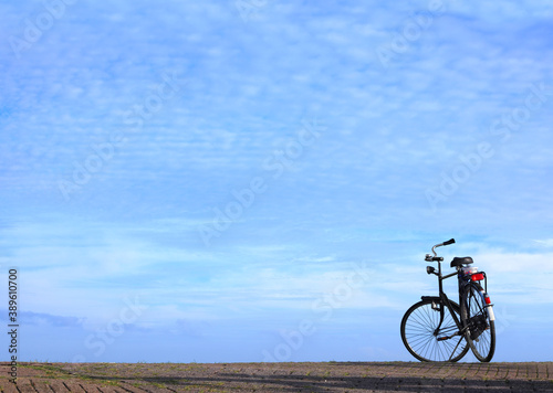 Bicycle parked on cobble stone road against magnificent blue sky over calm expanse on a sunny day. Netherlands. Minimalist image