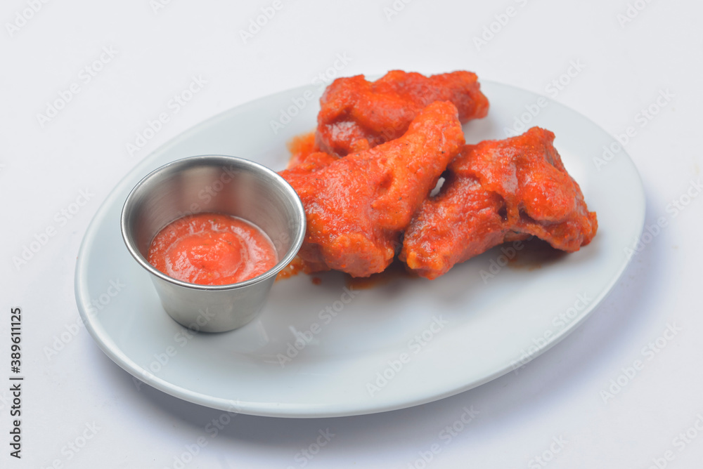 Buffalo chicken wings with tomato dip sauce. Served on a white plate over white background.