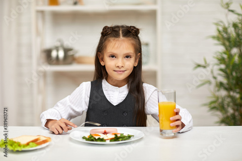 little child girl having breakfast - fried egg and orange juice in the kitchen. healthy breakfast. fried egg face smiles on a white plate