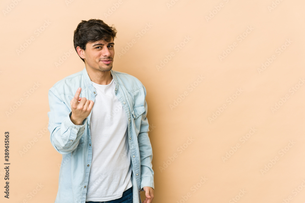 Young cool man pointing with finger at you as if inviting come closer.