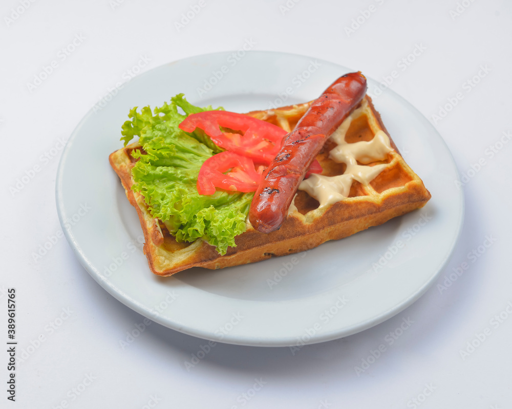 Sour waffle with fried sausage and vegetables on a plate. Delicious traditional breakfast idea. Belgian waffle recipe.