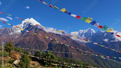 Several lines of colorful Buddhist prayer flags flying in the wind above Namche Bazar, Khumbu, Himalayas, Nepal with majestic mountain panorama in background including Thamserku peak (6,623 m). photo