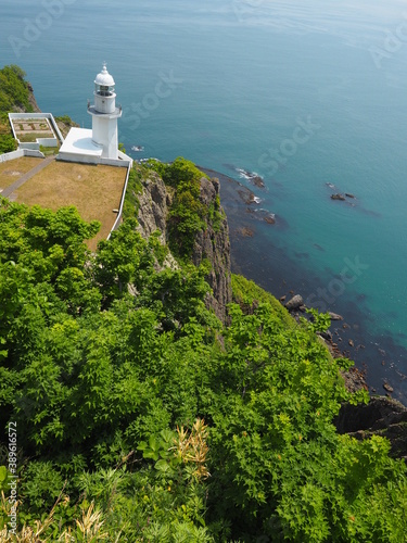 White lighthouse on a green hill above turquoise waters of Pacific Ocean on Misaki Pennisula in Hokkaido island, northern Japan