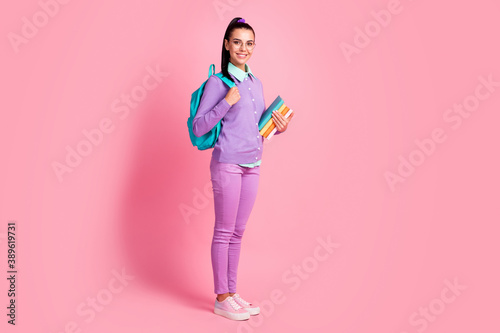 Full length photo of charming girl hold pile book wear specs backpack violet pullover pants sneakers isolated pink color background