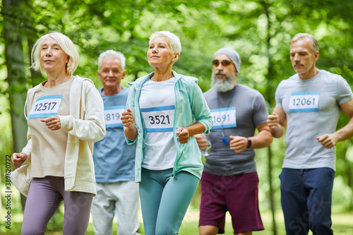 Active senior men and women spending summer day time together in park running marathon  medium long shot