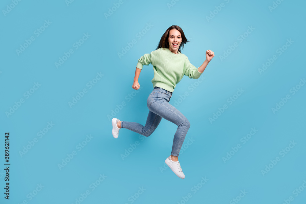 Full length body size side profile photo of laughing young girl running fast hurrying up jumping high smiling happily isolated on bright blue color background