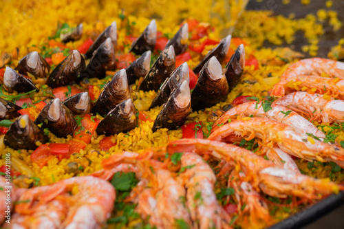 Cooked yellow paella with shrimp, mussel, rice, spice, saffron in huge paella pan at summer outdoor food market: close up. Spanish cuisine, seafood, gastronomy, street food concept