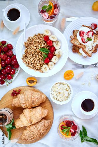Fresh and bright continental breakfast table, abundance healthy meal variety crunch cereal, french toast, fruits, lemonade, coffee, croissant on table served, top view, flat lay, copy space, frame..