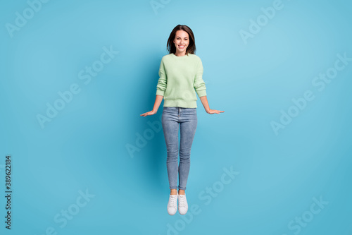 Full length body size photo of pretty jumping girl wearing casual outfit keeping hands along body smiling isolated on vibrant blue color background