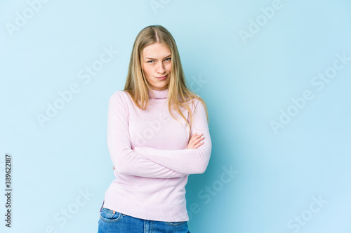 Young blonde woman isolated on blue background frowning face in displeasure, keeps arms folded. © Asier
