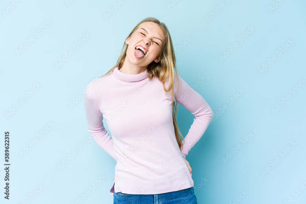 Young blonde woman isolated on blue background funny and friendly sticking out tongue. Young blonde woman isolated on blue background funny and friendly sticking out tongue.