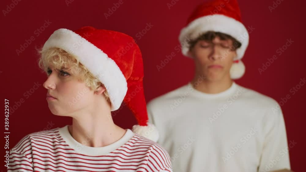 Young offended sad cute girl with her brother on the background in christmas santa hat isolated over red wall background Young offended sad cute girl with her brother on the background in christmas santa hat isolated over red wall background