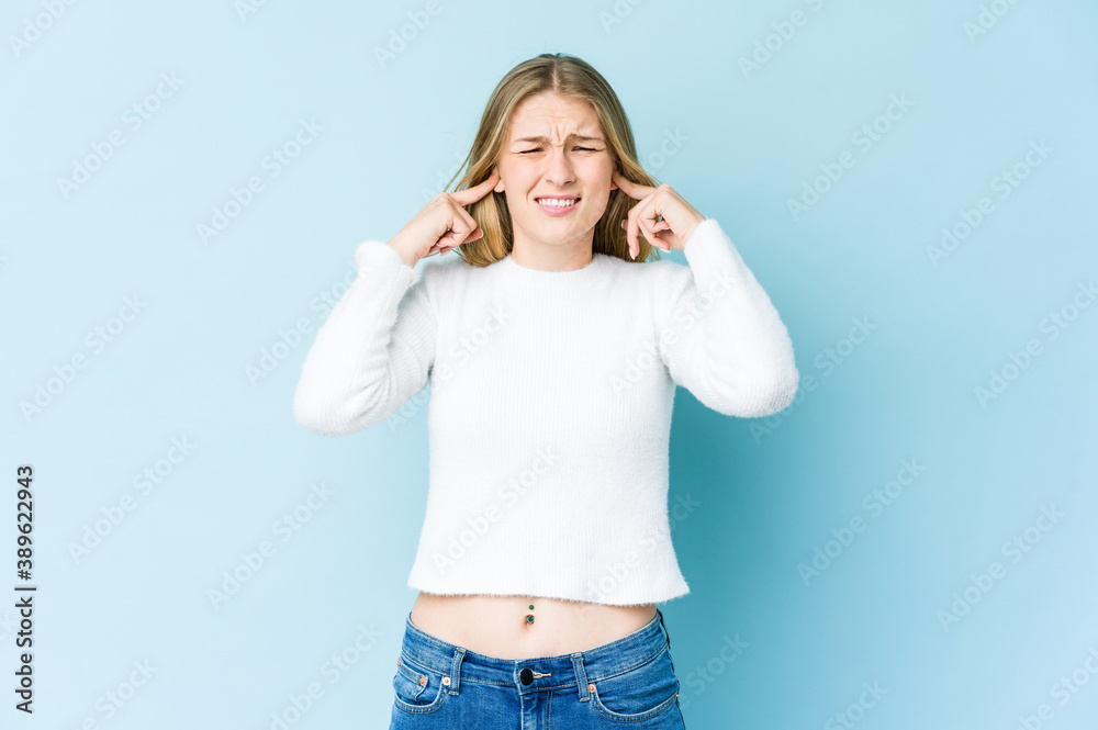 Young blonde woman isolated on blue background covering ears with fingers, stressed and desperate by a loudly ambient. Young blonde woman isolated on blue background covering ears with fingers, stressed and desperate by a loudly ambient.