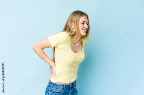Young blonde woman isolated on blue background suffering a back pain. © Asier