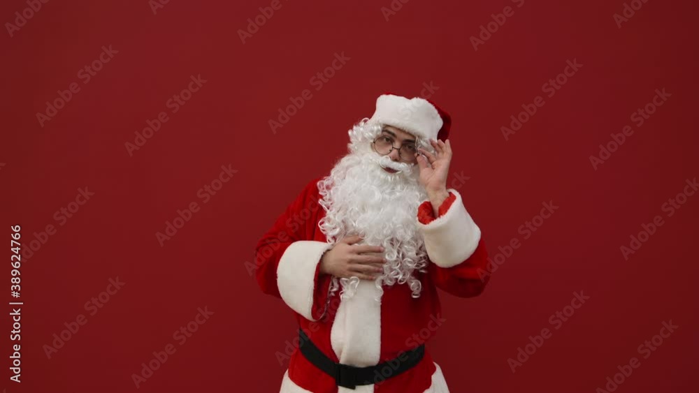 Puzzled Santa stands on a red background and spreads his arms to the side, looking confused at the camera. Christmas concept. Puzzled Santa stands on a red background and spreads his arms to the side, looking confused at the camera. Christmas concept.