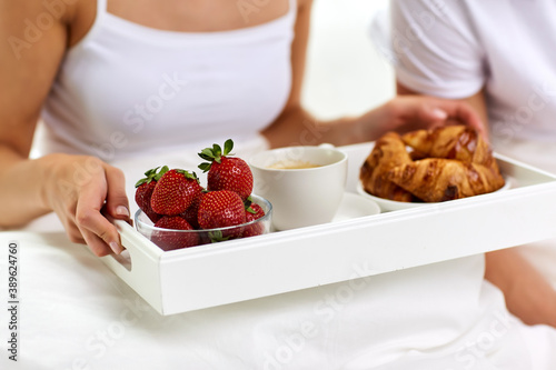 food and people concept - couple having strawberries  coffee and croissants for breakfast in bed at home