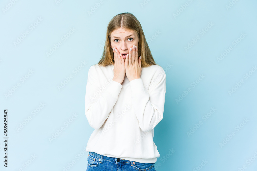 Young blonde woman isolated on blue background shocked, covering mouth with hands, anxious to discover something new. Young blonde woman isolated on blue background shocked, covering mouth with hands, anxious to discover something new.