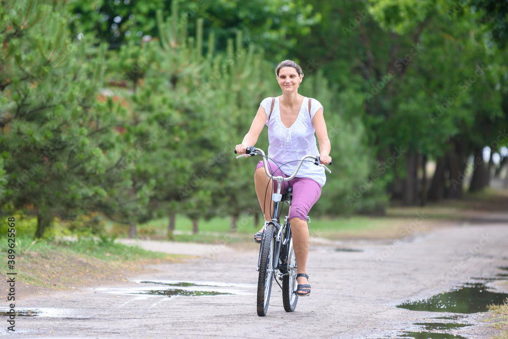 Naklejka premium Girl riding a bicycle on a rainy warm summer morning