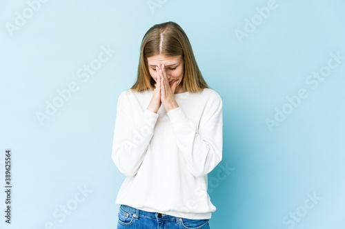 Young blonde woman isolated on blue background praying, showing devotion, religious person looking for divine inspiration. © Asier