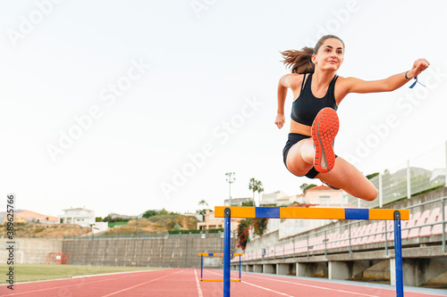 Fit female teenager athlete hurdler running jumping over hurdles - Copy space