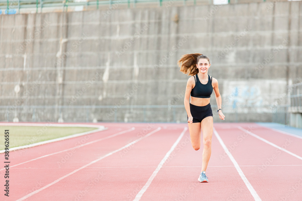 Smiling fit female teenager runner training on running track