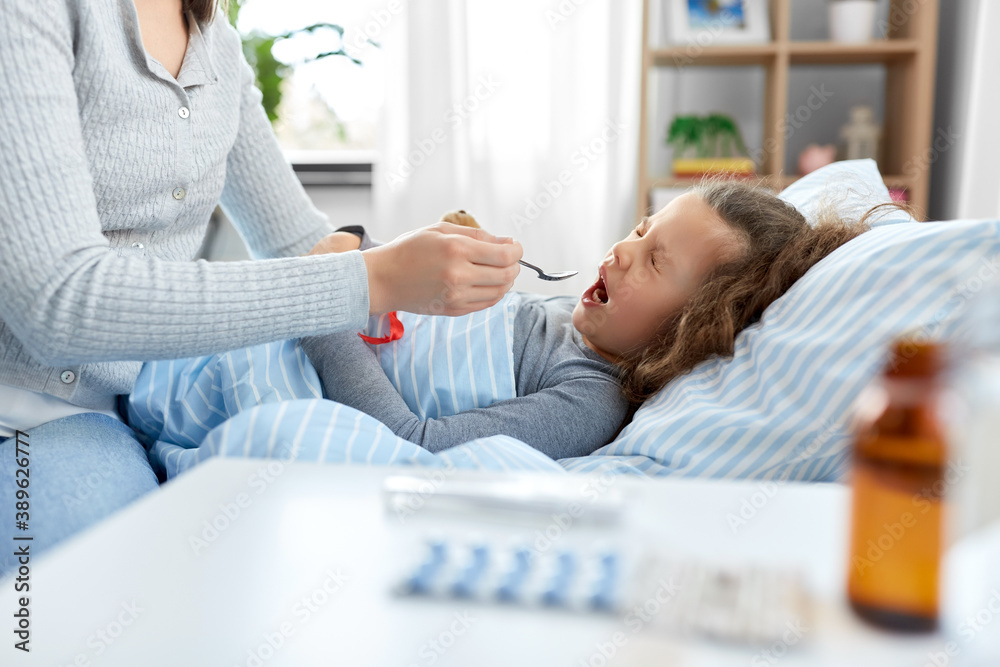Obraz premium family, health and medicine concept - mother giving cough syrup to little sick daughter lying in bed at home
