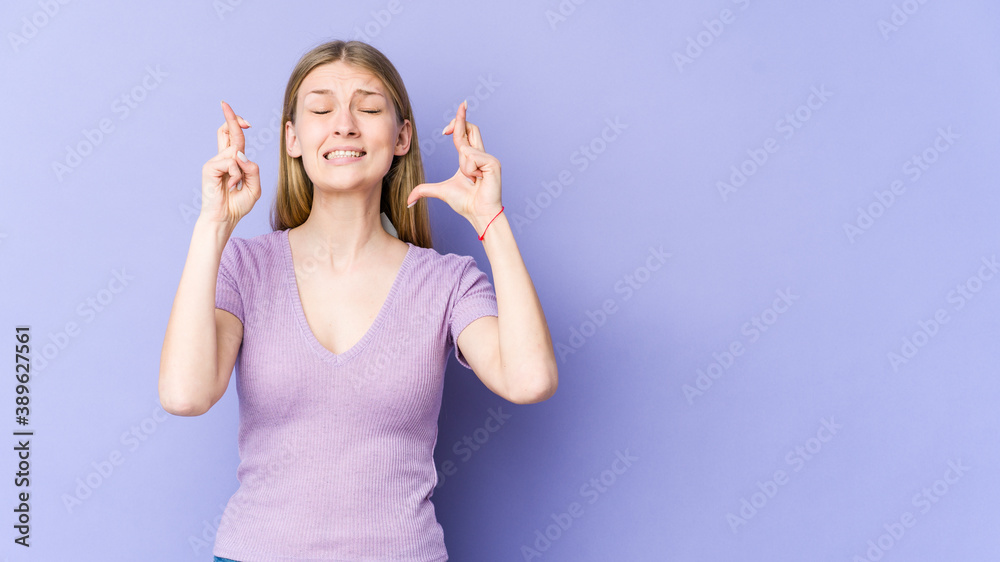 Young blonde woman isolated on purple background crossing fingers for having luck