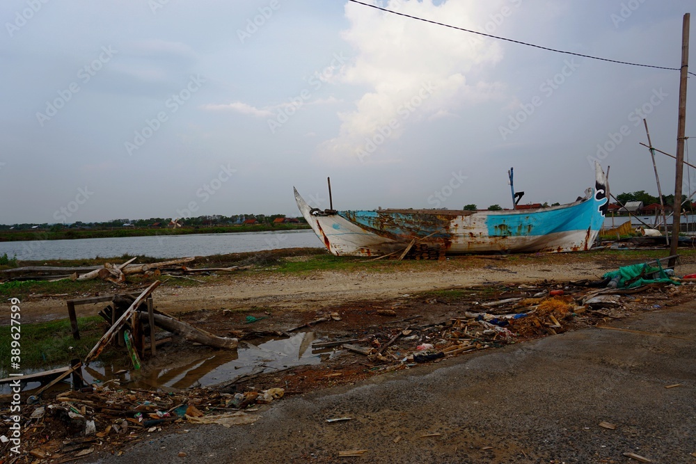 Fototapeta premium A broken boat parked on the beach under the blue sky adds to the beauty of the beach, Lebak beach, Jepara. Indonesia
