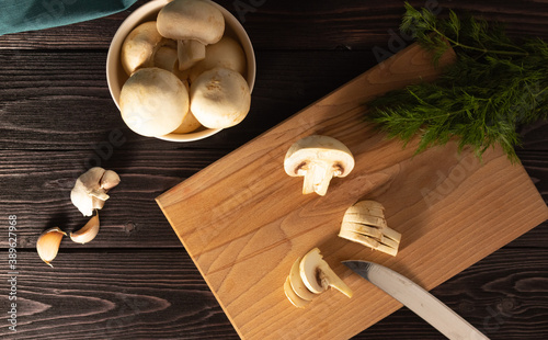 Chopped mushrooms on a wooden cutting Board. Dill, whole mushrooms in the background. Cooking vegetarian food. The view from the top.
