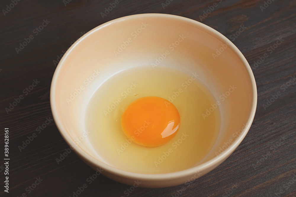Closeup of a Fresh Raw Egg Yolk and White in a Bowl Isolated on Wooden Table Closeup of a Fresh Raw Egg Yolk and White in a Bowl Isolated on Wooden Table