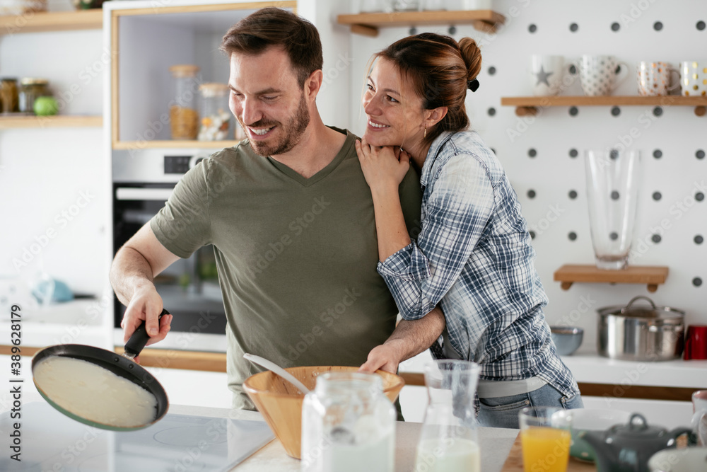 Husband and wife making pancakes at home. Loving couple having fun while cooking.. Husband and wife making pancakes at home. Loving couple having fun while cooking..