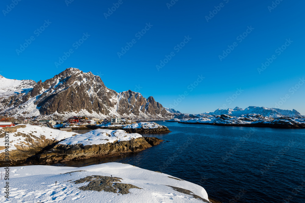 Beautiful winter landscape with sea and steep mountains near Svolvaer on the Lofoten islands in Norway with snow on clear day with blue sky