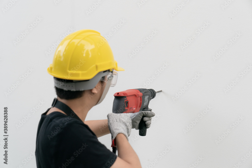 Man builder or worker with yellow helmet and goggle drilling machine on white wall. Man builder or worker with yellow helmet and goggle drilling machine on white wall.