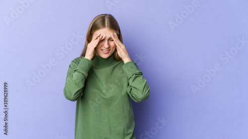 Young blonde woman isolated on purple background having a head ache, touching front of the face.