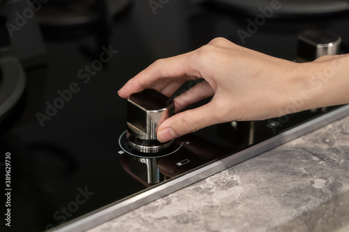 Woman hand turning switch knob on gas stove in kitchen.