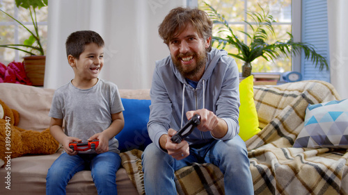 Father and son sitting on couch at home playing video game together