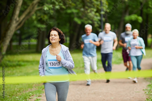 Active sporty mature woman with brown hair taking part in marathon race finishing it first, copy space