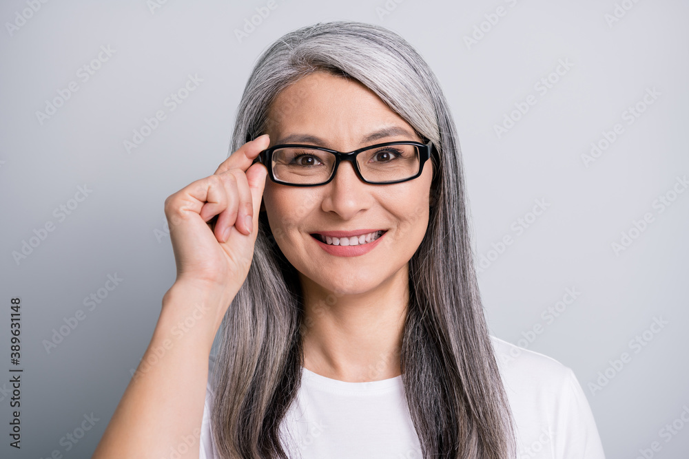 Photo of retired woman toothy smile look camera hold specs wear eyeglasses white t-shirt isolated grey color background Photo of retired woman toothy smile look camera hold specs wear eyeglasses white t-shirt isolated grey color background