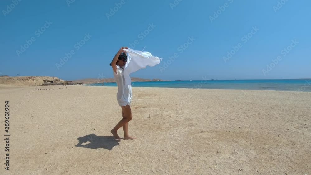 Woman on Giftun island, Hurghada, Egypt. Fashion model in white dress and hat enjoying breeze with scarf, slow motion Woman on Giftun island, Hurghada, Egypt. Fashion model in white dress and hat enjoying breeze with scarf, slow motion