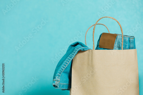 A paper craft bag with  blue jeans is on a blue background. Concept of thrift stores, resale, second hand. photo